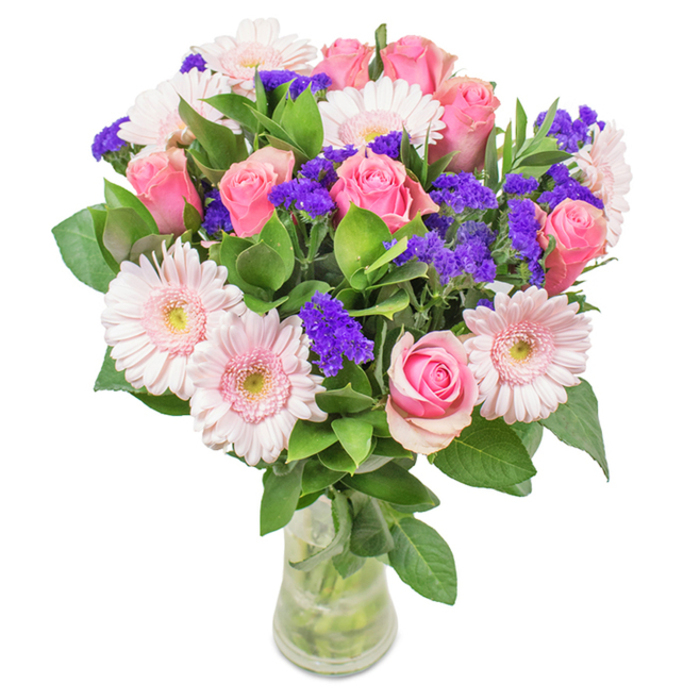 Displayed against a clean, white backdrop, this elegant floral ensemble captures the inviting spirit of Belmont with every detail. Approximately seven to nine pink roses, some just beginning to unfurl, form the heart of the arrangement, their classic spiral petals highlighted by the soft diffused light that feels like an early morning along Avenue Road. Five to seven pale pink gerbera daisies add a lively contrast, their broad, cheerful faces edged with nearly white centers, lending a gentle brightness that echoes the welcoming lawns of Belmont Park. Dotted throughout are clusters of vivid purple statice, each one bursting with colour and a tang of wild spice, bringing depth and an uplifting accent to the display. Lush, glossy green foliage wraps around the bouquet, enhancing both the texture and the plentiful feeling of abundance. All stems are gathered in a transparent glass vase, the water clear and inviting, showcasing the arrangement's fresh-from-the-garden essence-akin to a beautiful gift hand-delivered by Flower Delivery Belmont to homes around the village. Perfect for birthdays, anniversaries, Mother's Day, or as a thoughtful touch to home or office, this bouquet imparts an unmistakable sense of joy, local pride, and heartfelt celebration to every setting.